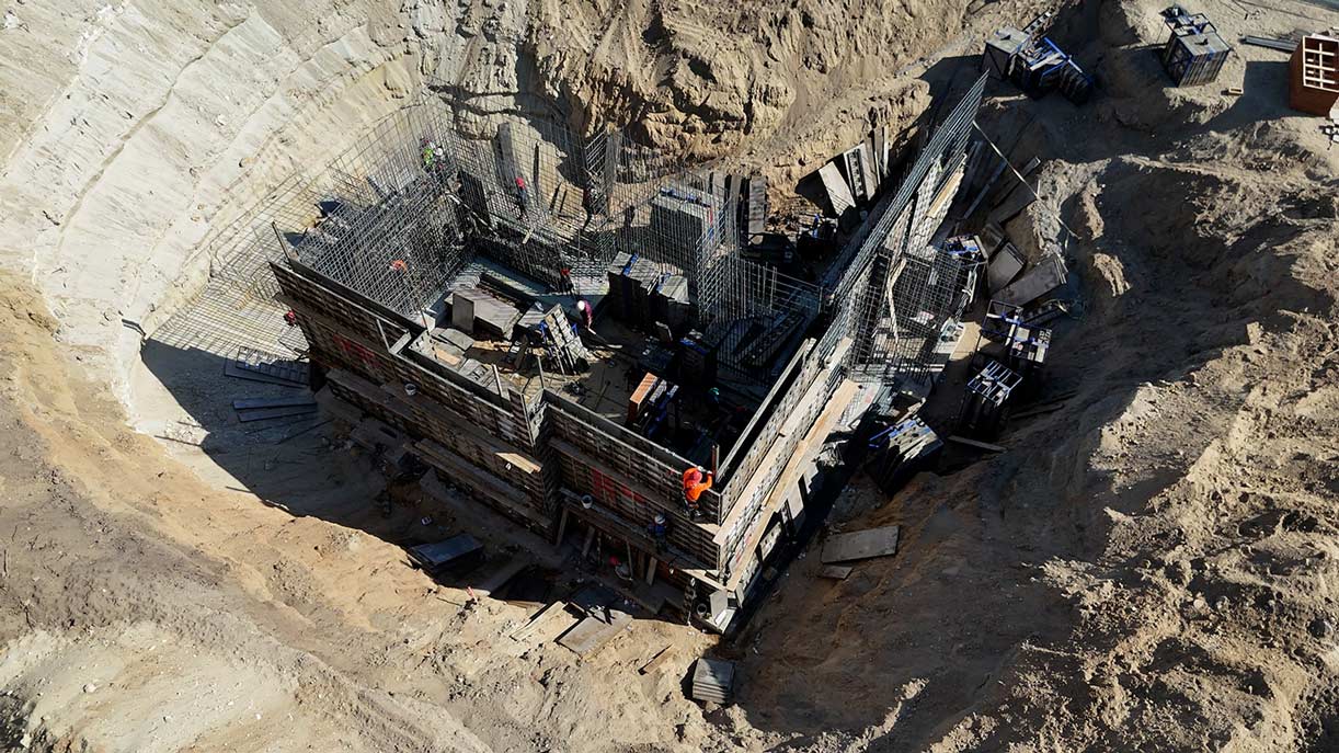 Workers climbing stacked aluminum form panels for tall foundation wall build by Utah concrete contractor
